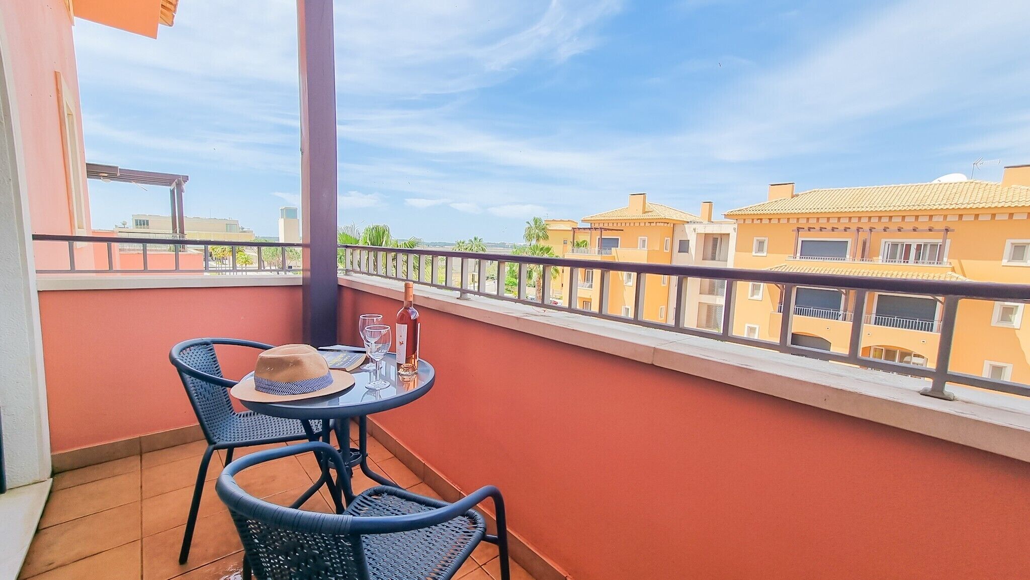 Een balkon met een tafel, stoelen, een fles en glazen.