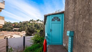 A turquoise door with a small wooden staircase leading up to it, surrounded by greenery and overlooking a hillside with buildings. - Studio Apartment 'Little California' with Private Terrace, Wi-Fi and Air Conditioning (Cagnes-sur-Mer)