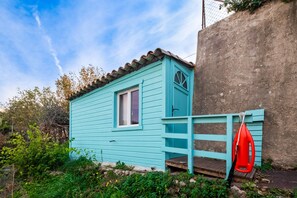 Uma pequena cabana de madeira azul clara, com janela, porta e um pequeno alpendre.