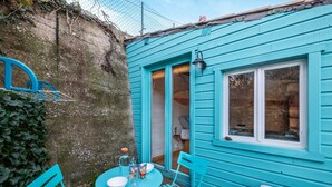 A turquoise cottage with a small patio, a table with chairs, and a window. - Studio Apartment 'Little California' with Private Terrace, Wi-Fi and Air Conditioning (Cagnes-sur-Mer)