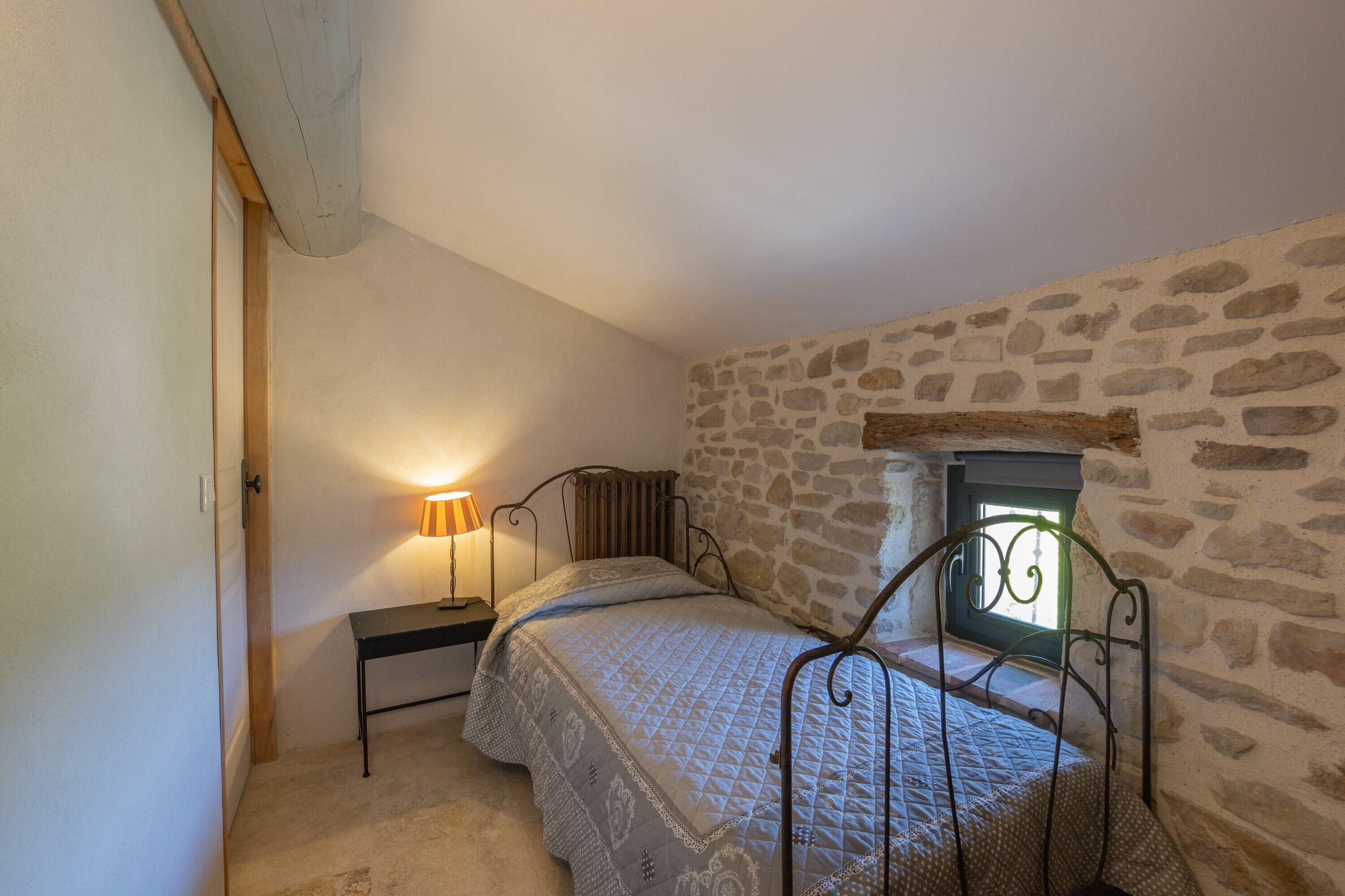 Una camera da letto con parete in pietra, un letto con struttura in metallo, un comodino con una lampada e una finestra vista.