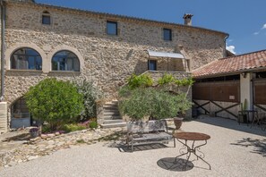 Un edificio in pietra con finestre ad arco, un cortile in ghiaia e una panchina in legno con un tavolo in metallo.