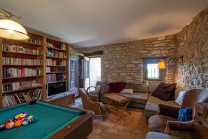 Un accogliente soggiorno con tavolo da biliardo, una poltrona, una sedia e una libreria piena di libri.
