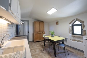 A kitchen with a sink, cabinets, a dining table with chairs, and a window with a stone frame. - Holiday Home 'Gîte L'olivier Au Mas Dujau' with Shared Pool, Private Terrace and Wi-Fi (Saint Sauveur de Cruzières)