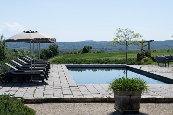 A swimming pool with lounge chairs and umbrellas, surrounded by a landscaped area with a view of distant hills. - Holiday Home 'Gîte L'olivier Au Mas Dujau' with Shared Pool, Private Terrace and Wi-Fi (Saint Sauveur de Cruzières)