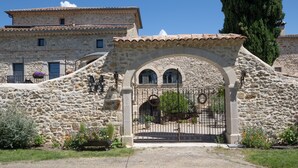 Un edificio de piedra con entrada protegida por una reja, ventanas arqueadas y tejado de tejas.