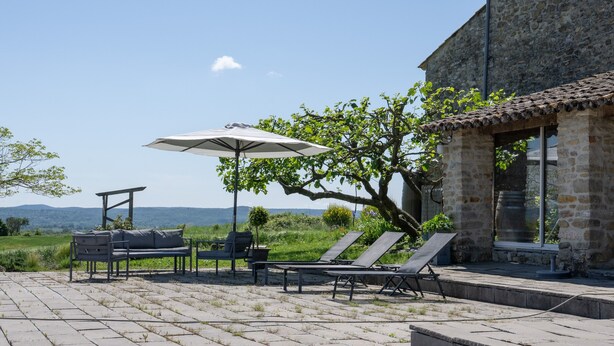 Un patio con muebles de exterior, un paraguas grande y un edificio de piedra con una ventana.