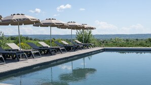 Un área de piscina con sillas de descanso y sombrillas, cielo despejado y vistas distantes de colinas.