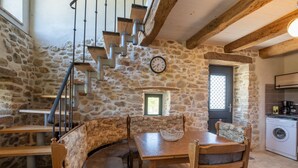 Una habitación con paredes de piedra, una mesa de comedor, sillas, un reloj y una escalera.