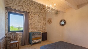Un dormitorio con pared de piedra, una silla de madera, un aparador, un radiador y una cama.