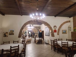 Ein Restaurant mit mehreren Tischen, einer Kandelaber und steinernen Bögen.