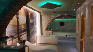 Une pièce aménagée comme un spa, avec un canapé blanc aux lignes courbes, un comptoir d’accueil et un mur en pierre agrémenté d’une alcôve illuminée de lumière verte.
