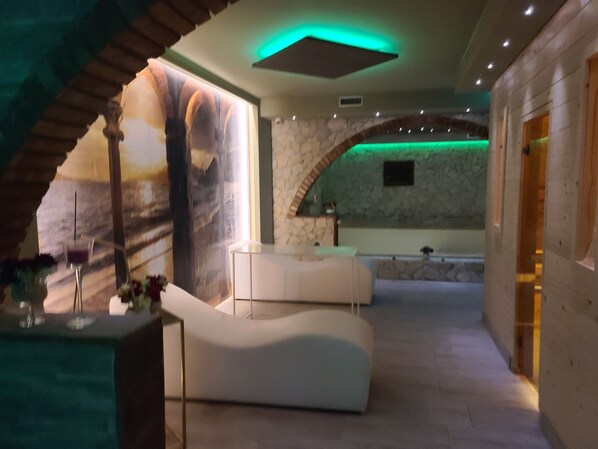 Um espaço tipo spa com um sofá branco curvo, um balcão de recepção e uma parede de pedra com um nicho iluminado em verde.