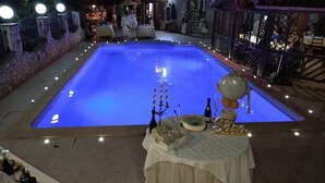 Une piscine éclairée de lumière bleue, entourée de murs en pierre et de tables ornées d’objets décoratifs.