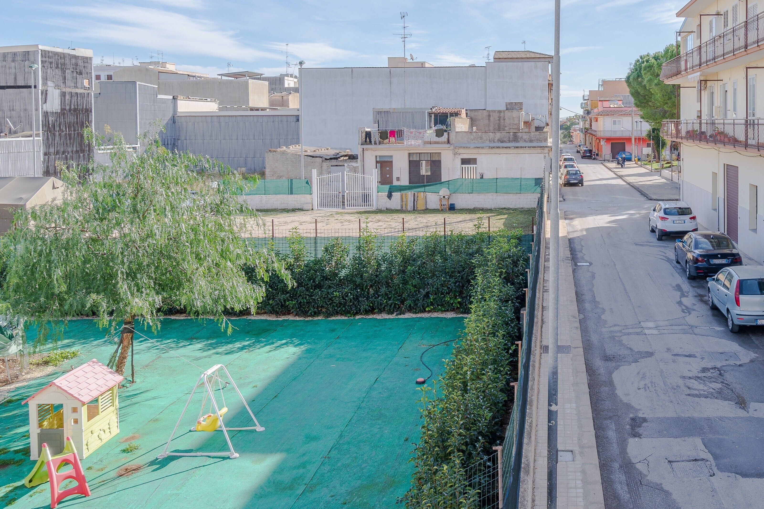 Ein Wohngebiet mit einem Spielplatz, einem verschlossenen Eingangsbereich und parkenden Autos an der Straße.