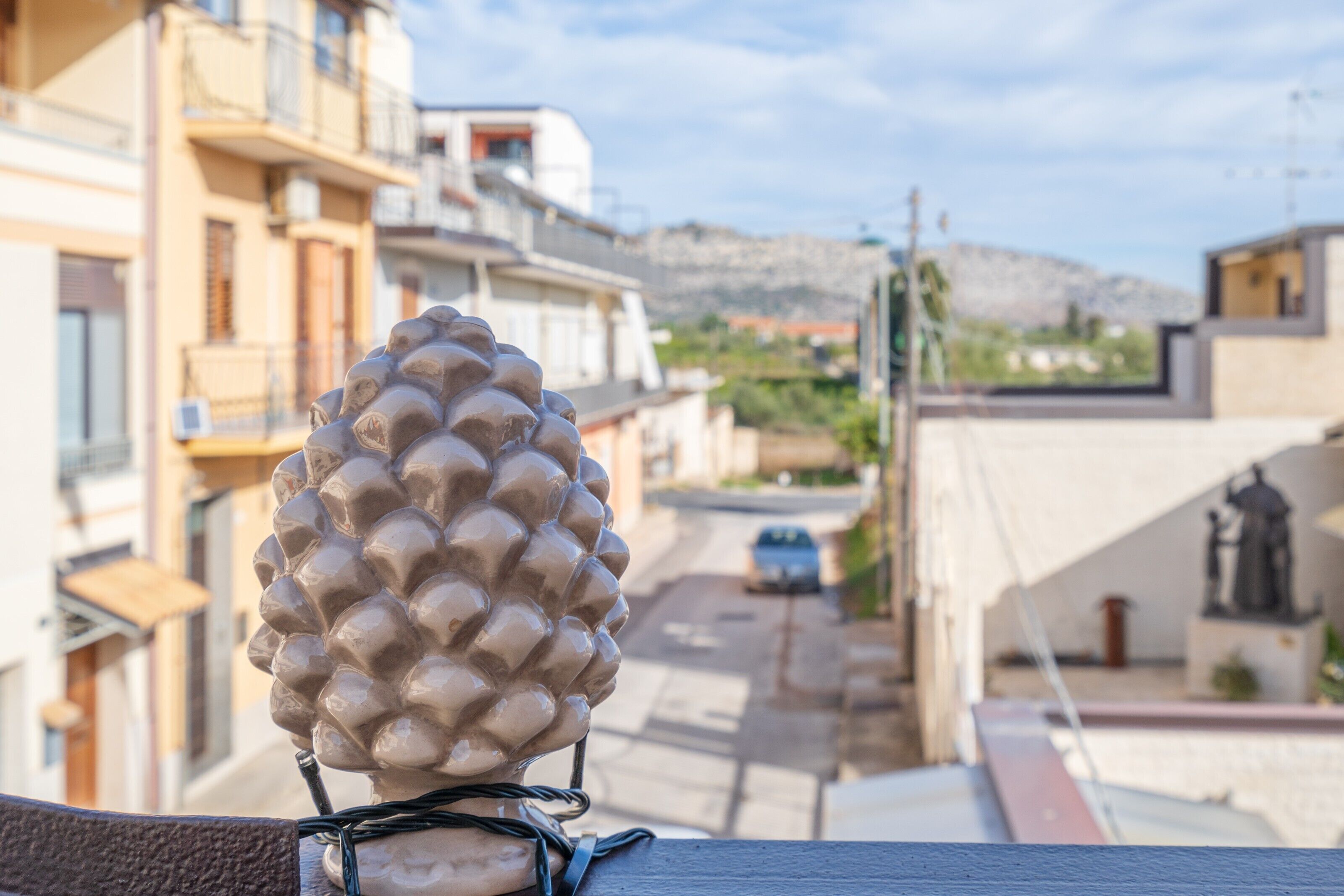 Una escultura de piña en un balcón con vistas a una calle con edificios y una colina distante.