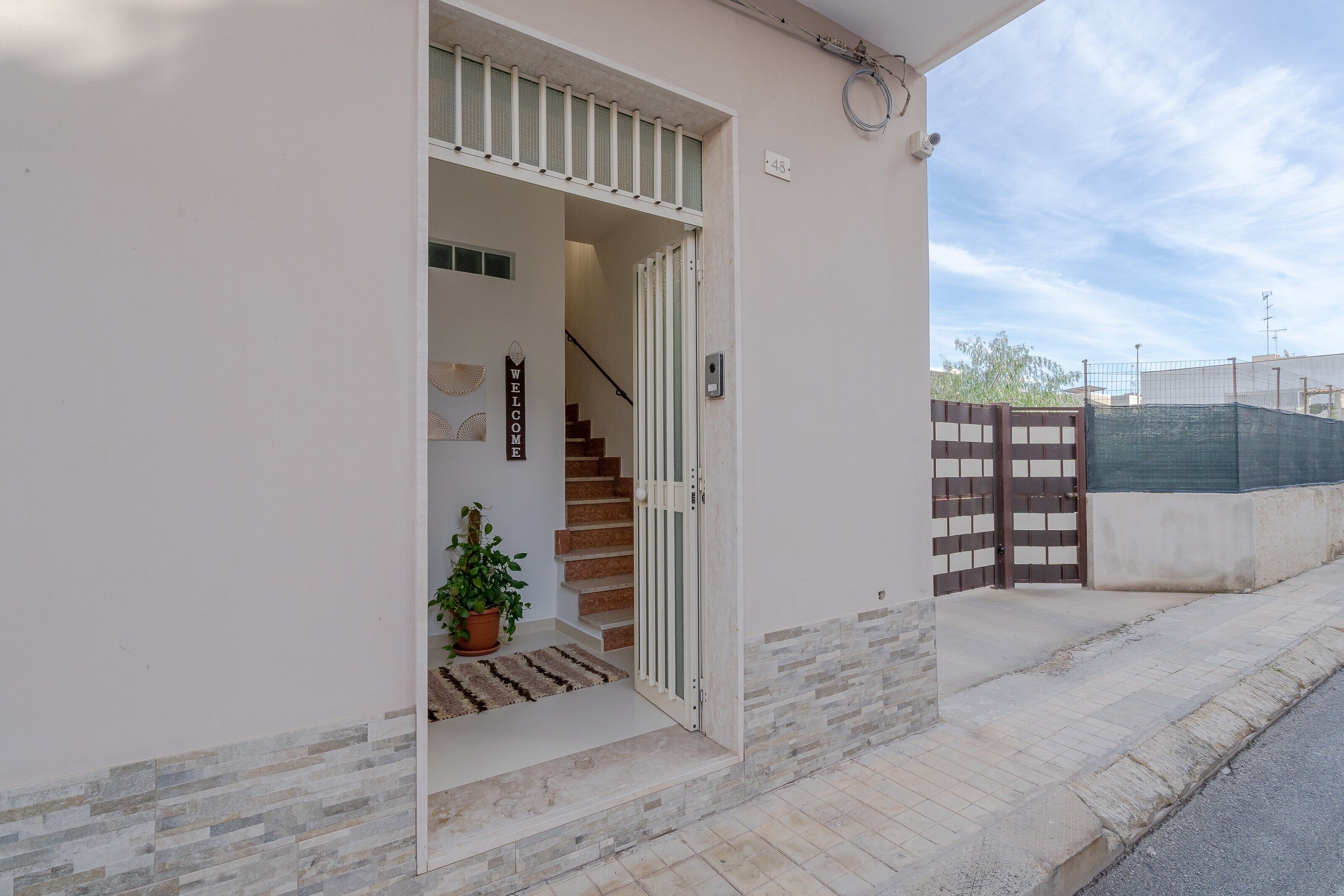 A residential entrance with a staircase, a welcome mat, and a potted plant.