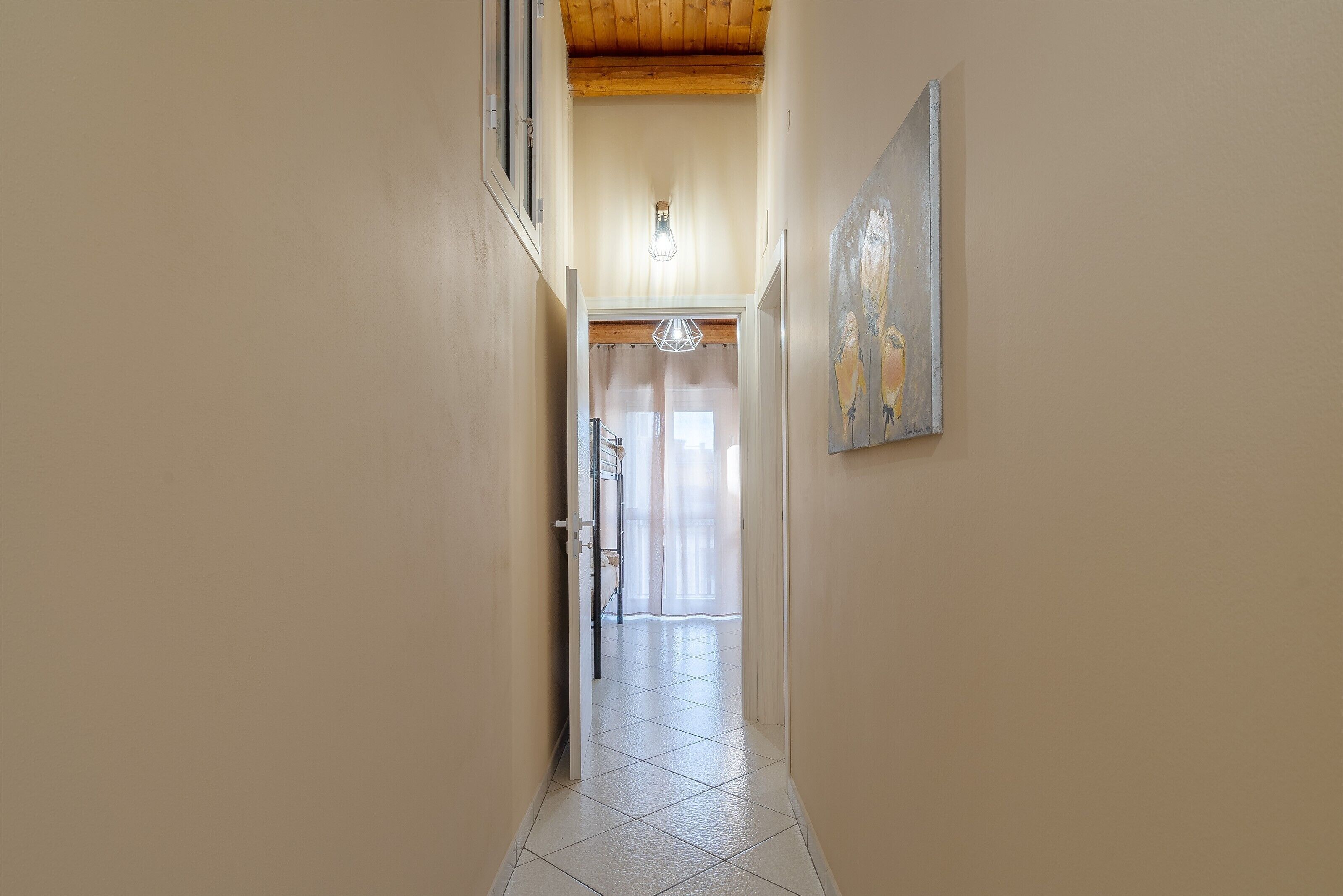 A hallway with a tiled floor, a light fixture, and a painting on the wall.