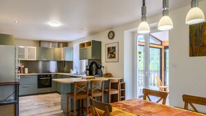 A modern kitchen with a central island, wooden chairs, and a dining table with a patterned tablecloth. - Holiday Home 'Gîte La Ramée' with Mountain View, Private Terrace and Wi-Fi (BAN SUR MEURTHE CLEFCY)