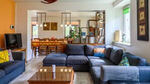 A living room with a sofa, a coffee table, and a television. There is a dining area with a table and chairs. - Holiday Home 'Gîte La Ramée' with Mountain View, Private Terrace and Wi-Fi (BAN SUR MEURTHE CLEFCY)