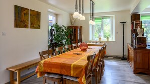 A dining area with a long table, chairs, pendant lights, a wooden cabinet, and a large plant. - Holiday Home 'Gîte La Ramée' with Mountain View, Private Terrace and Wi-Fi (BAN SUR MEURTHE CLEFCY)