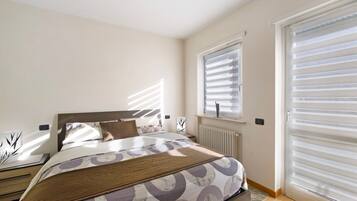 Ein Schlafzimmer mit Bett, Heizkörper, Fenster mit Jalousien und Tür mit Schiebesystem.