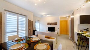 A modern dining area with a black table set for four, a television on a stand, and a kitchen area with a refrigerator and microwave. - Apartment 'Appartamento Da Jenny' with Mountain View, Balcony and Wi-Fi (aosta)