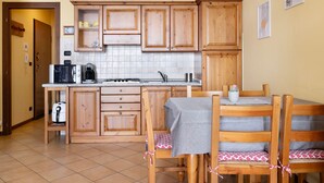 Eine Küche mit Holzschränken, einem Esstisch mit Stühlen und einer Kaffeemaschine.