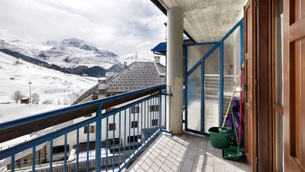 Ein Balkon mit Blick auf schneebedeckte Berge, einer Beton Decke und einer Holztür.
