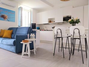 Una sala de estar moderna con un sofá azul, una mesita blanca con una cesta y dos sillas blancas.