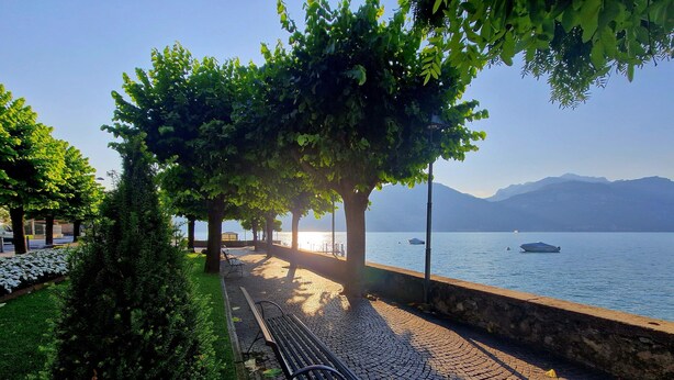 A paved walkway with benches, trees, and a view of a lake with boats. - Apartment 'Vichi's Nest' with Lake View, Wi-Fi and Air Conditioning (Pianello Del Lario)