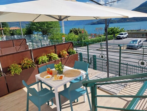 A balcony with a table, chairs, and a view of a lake and mountains.