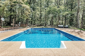 A rectangular swimming pool with a clear blue water, surrounded by a pebble deck and a brick wall.