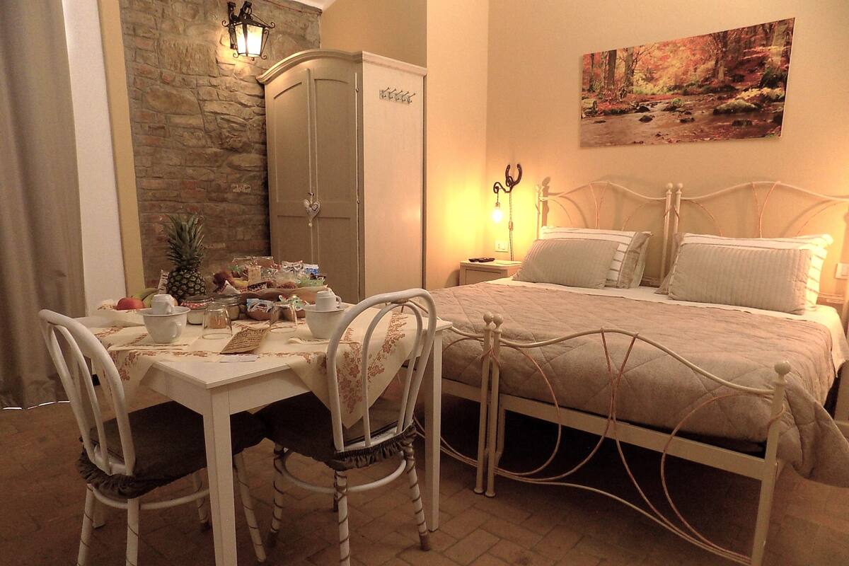 A bedroom with a bed, bedside tables, a nightstand, a lamp, a painting, and a stone wall.