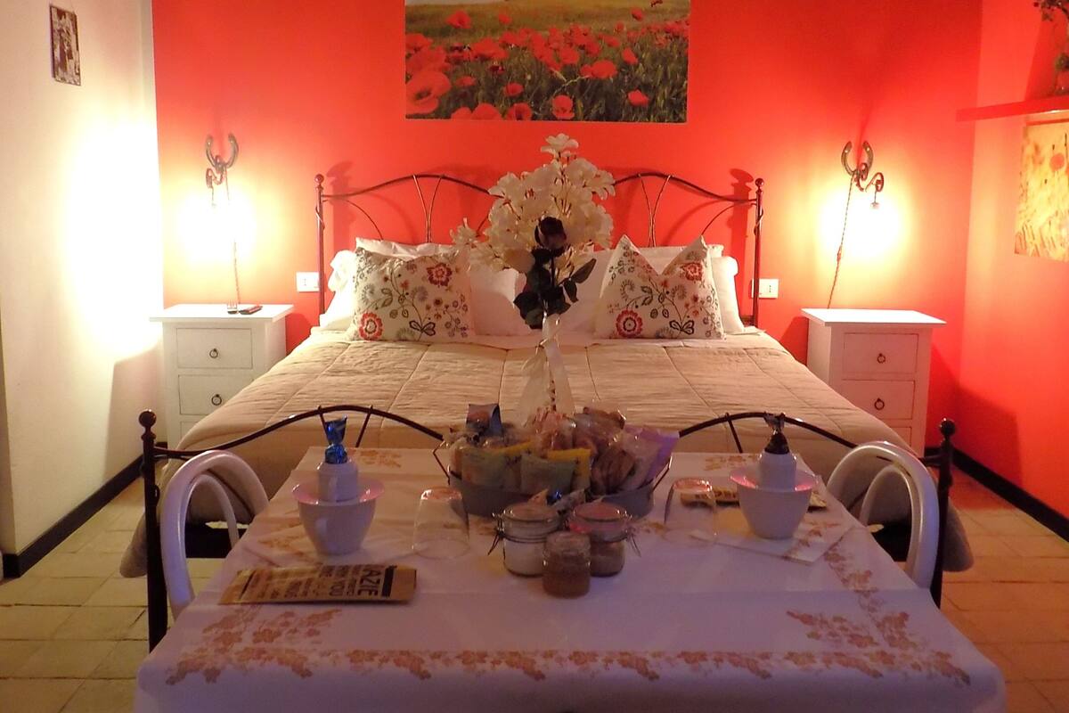 A bedroom with a bed, bedside tables, a table with a vase of flowers, and a painting on the wall.