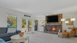 Una sala de estar con chimenea de piedra, un televisor montado arriba y un letrero que dice "LAKE HOUSE".