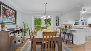 Cocina moderna con comedor, que incluye una mesa de madera, sillas, una isla de cocina y un amplio ventanal con vistas a la vegetación.