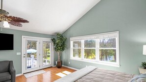 A bedroom with a bed, a gray armchair, a ceiling fan, a large window, and a potted plant. - Huge Lakehouse w/Pool, Hot Tub & Fire Pit Near Nashville! (Hendersonville)