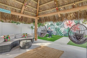 A covered outdoor seating area with a thatched roof, wicker furniture, and hanging chairs.