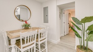 A dining area with a wooden table and white chairs, a round mirror on the wall, and a potted plant. - Heated Pool + Backyard: North Palm Beach Retreat! (North Palm Beach)