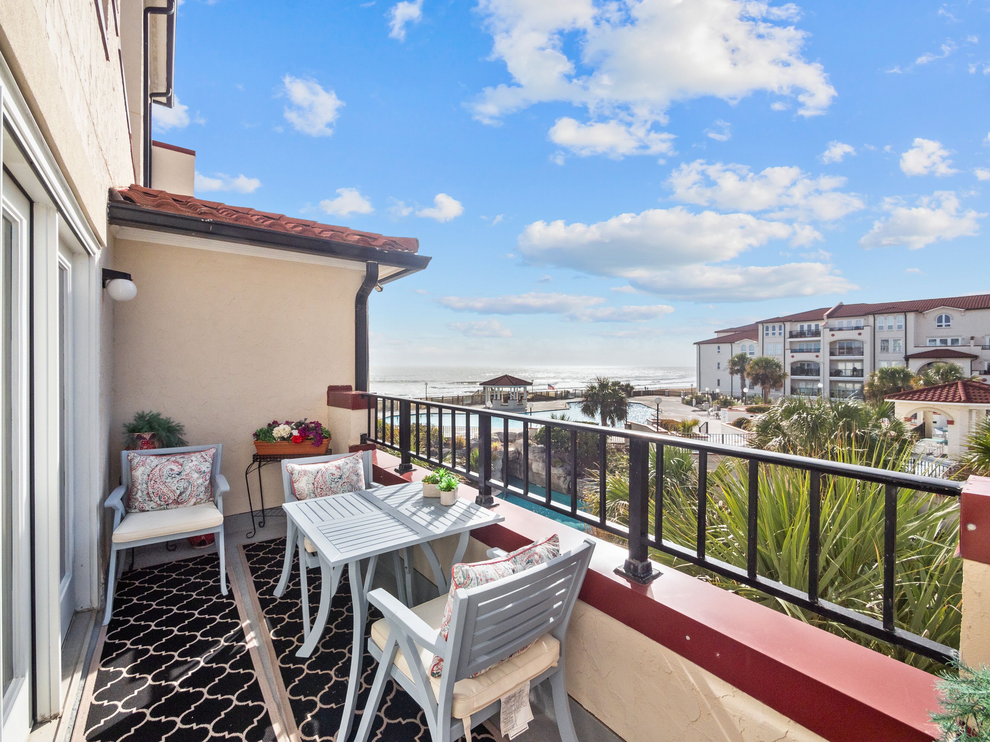 A balcony with a table and chairs, overlooking a beach and a resort area.