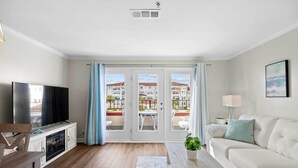 A living room with a flat-screen TV, a sofa, a coffee table, and a dining area with a table and chairs. - North Topsail Beach Condo in Resort-Style Complex! (North Topsail Beach)