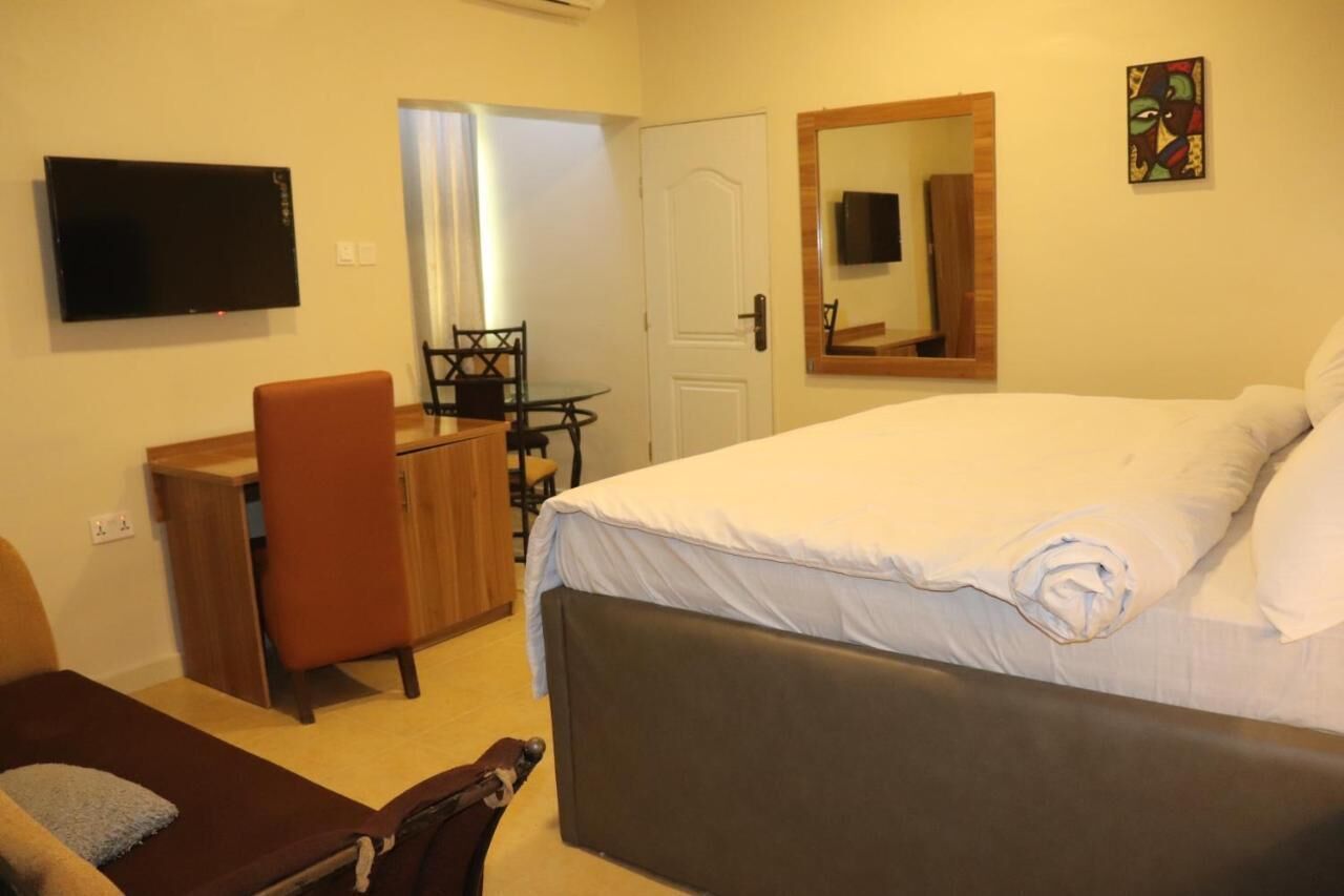 A hotel room with a bed, a desk, a chair, a TV, and a door.
