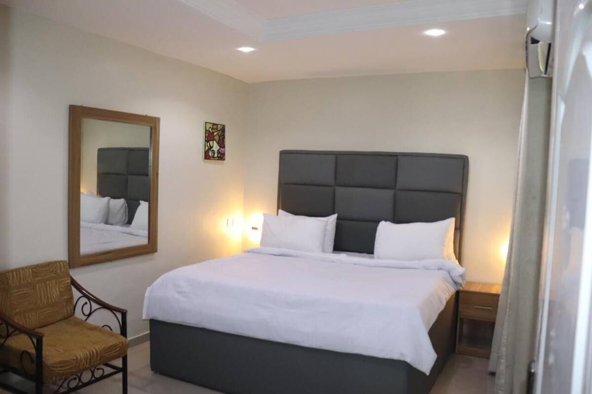 Ein Schlafzimmer mit einem großen Bett, einem Sessel, einem Nachttisch, einem Spiegel und einem Wandbild.
