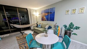 Una sala de estar moderna con un sofá, una mesa de comedor con sillas, una hamaca y un ventanal con cortinas.