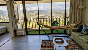 Una habitación con balcón, una hamaca, un sillón verde, un sofá y una alfombra estampada.