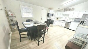 A modern kitchen with white cabinets, a microwave, and a refrigerator. There is a dining area with a table and chairs. - Peace in the City (Decatur)