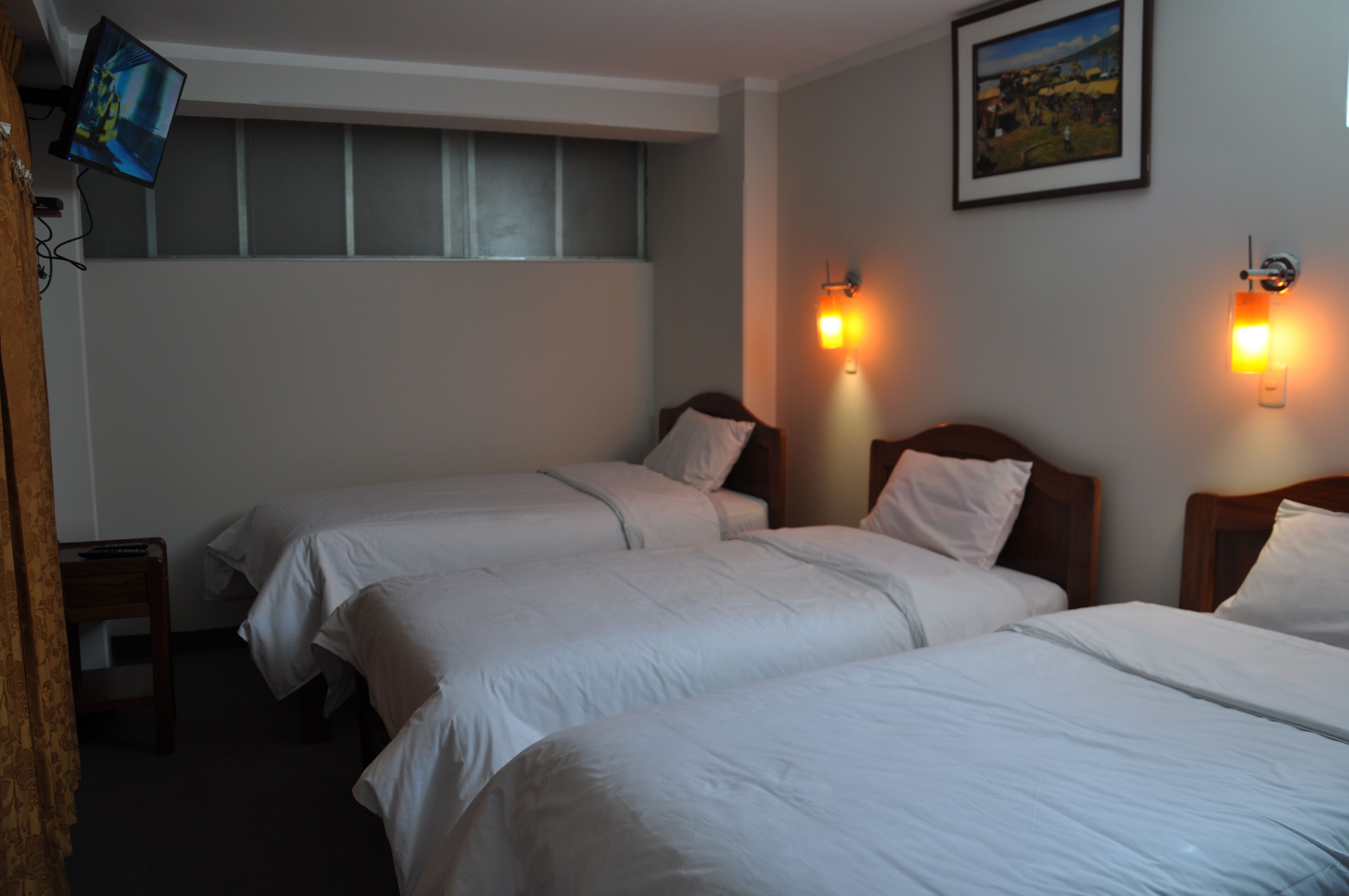 A hotel room with two single beds, a small table, a TV, and two wall-mounted lights.