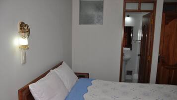 A bedroom with a bed, a nightstand, a wall-mounted light, and a door leading to a bathroom.