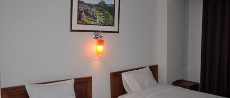 Habitación de hotel con dos camas, una mesita de noche, una lámpara de pared y un cuadro en la pared.